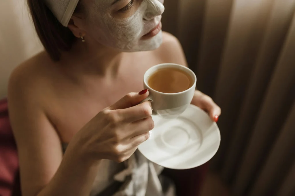 Woman enjoying detox tea during a self-care routine with a face mask