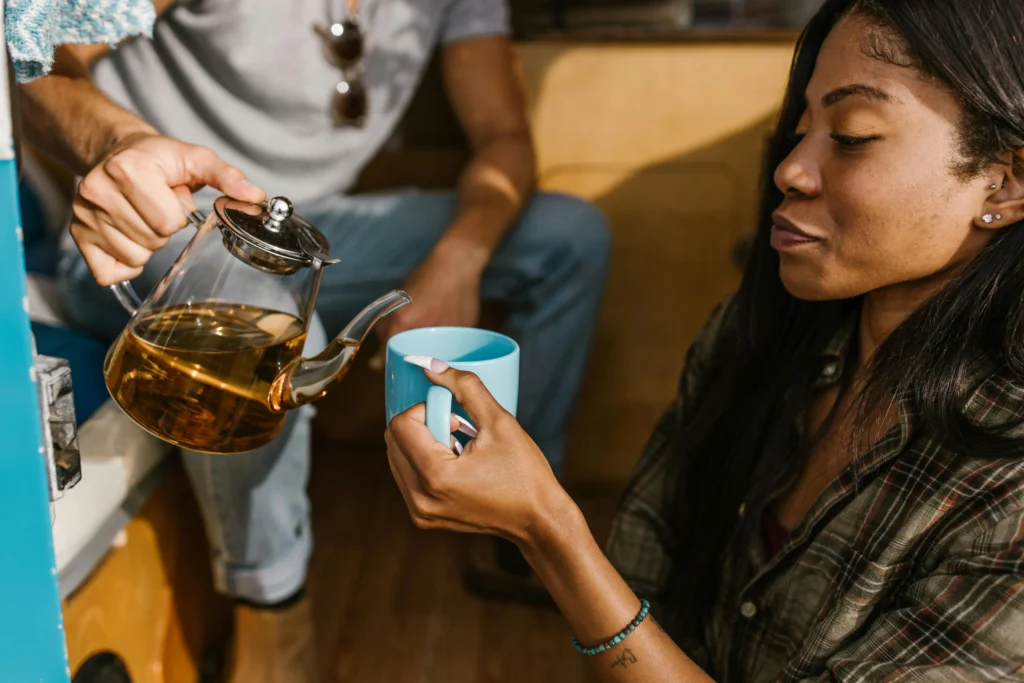 Woman holding a blue mug while herbal detox tea is being poured from a glass teapot
