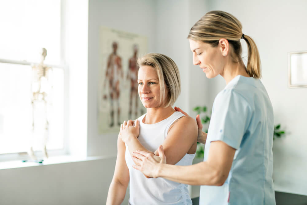 Physiotherapist examining a woman's shoulder and elbow for joint pain.