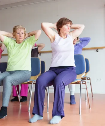 Seniors practicing seated chair yoga twist in a group class