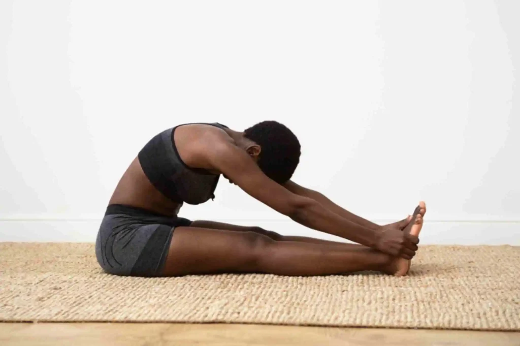 Person in Seated Forward Fold (Paschimottanasana) reaching toward feet to stretch the spine and hamstrings for relaxation and stress relief.