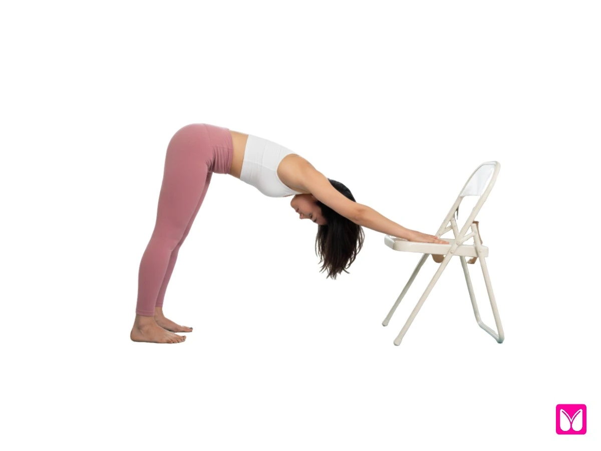 A woman practicing a simplified Downward Dog using a chair for support, demonstrating how simple yoga poses can decompress the spine.